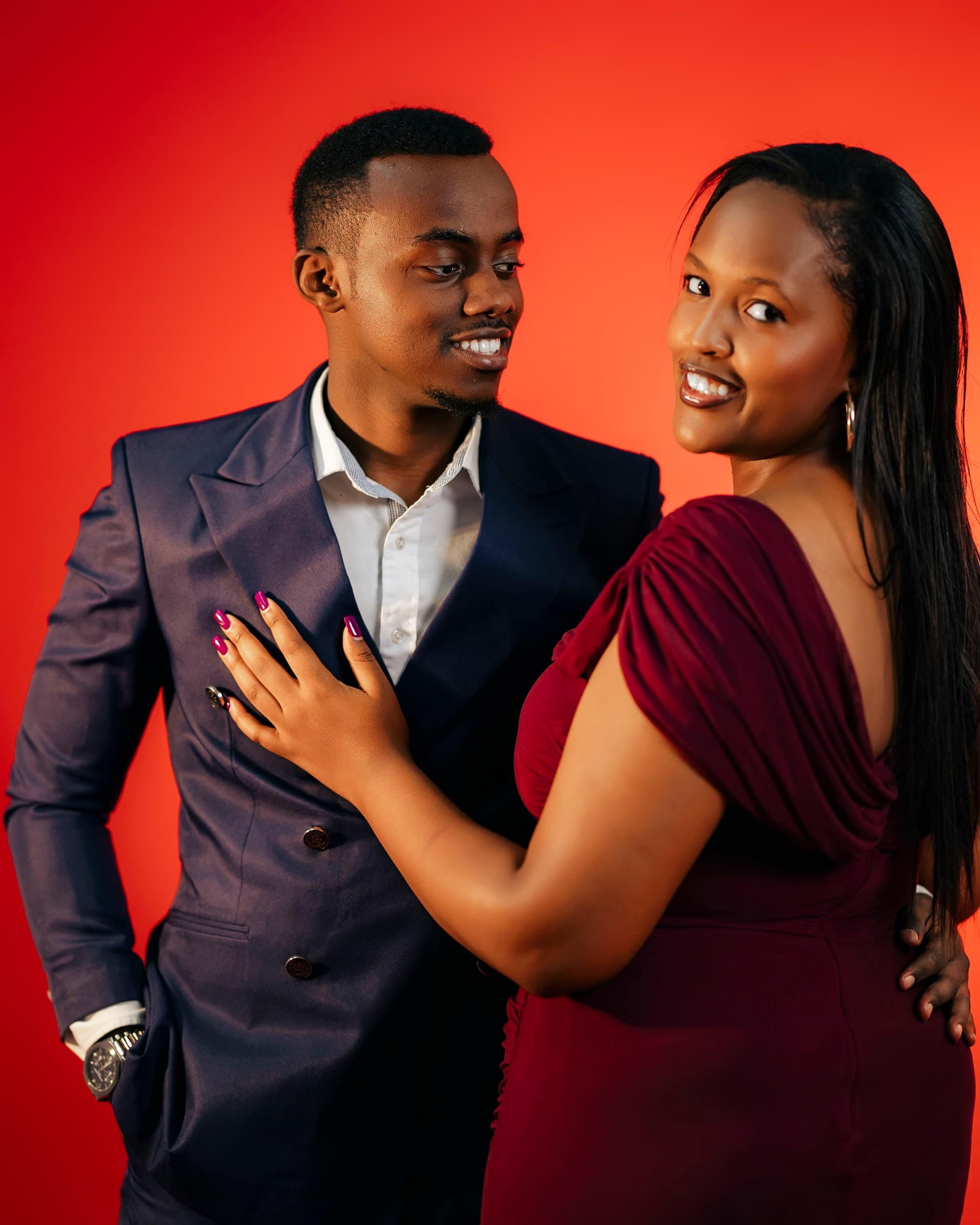 Alisiane and Tristan smiling at each other against a warm red backdrop